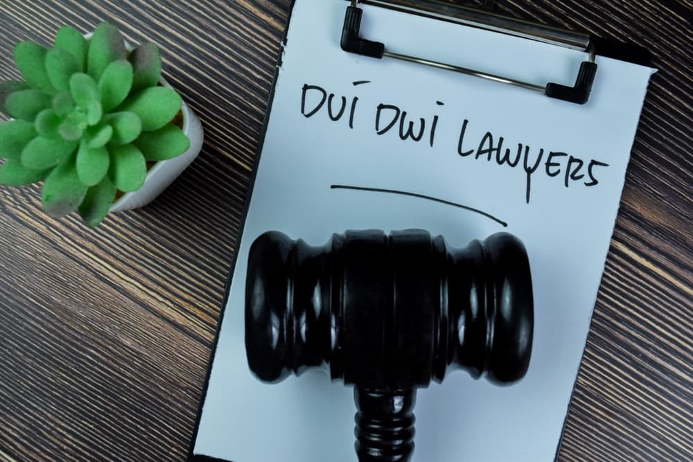 Legal professionals specializing in cases involving driving under the influence or driving while intoxicated are depicted writing on paperwork beside a gavel, set upon a wooden table.