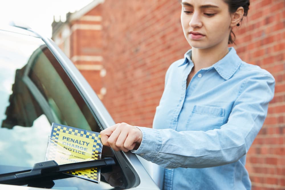 A young girl, visibly frustrated, glances at a parking ticket on his windshield.
