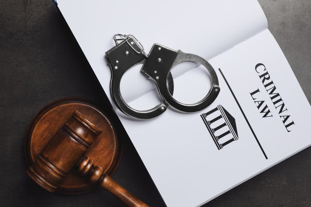 A flat lay image featuring a judge's gavel, handcuffs, and a book on criminal law against a grey background.