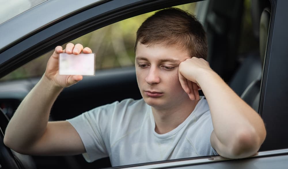 The driver, visibly upset and driving recklessly, extends their driver's license out of the car window during a police check control.