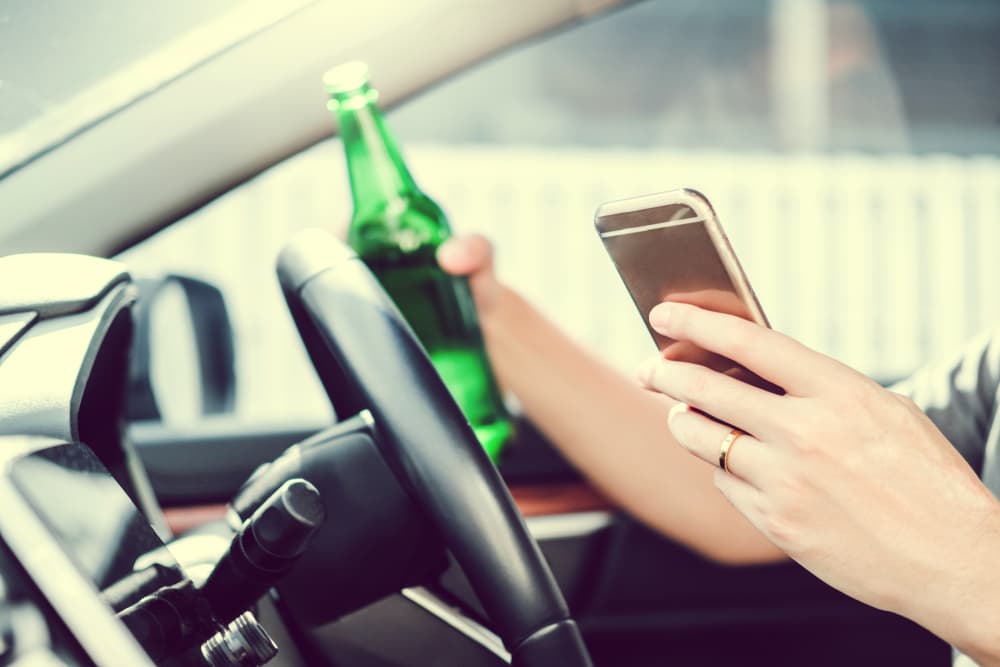 A man driving dangerously on the road while holding a bottle of beer, illustrating drunk driving risks.