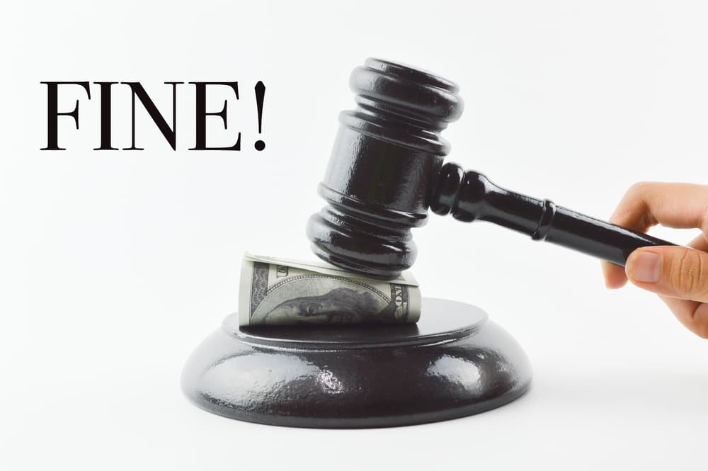 Front view of judge's gavel and money banknotes over a white background with the text "FINE!" written in bold.