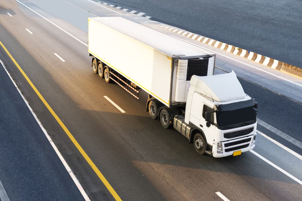 White truck on a highway transporting a container, representing the logistics of import and export. Concept of industrial land transportation.