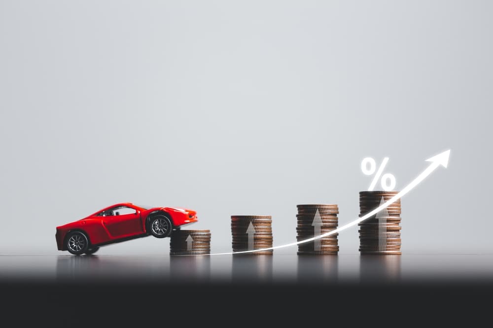 Stacks of coins and red car with percentage symbol for increasing insurance rates